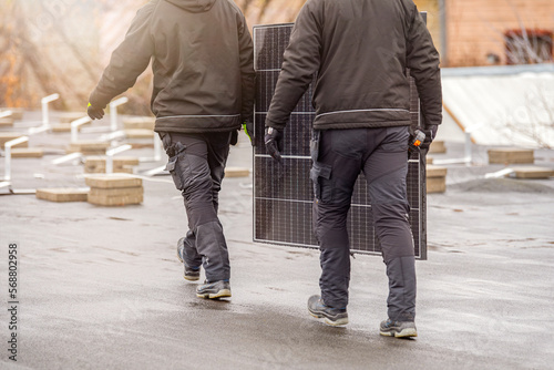 The process of installing solar panels. Solar panel installers work on the roof. Installers carry solar panel module to installation site, green and renewable energy concept