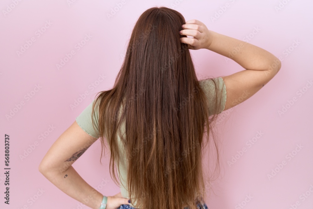 Beautiful brunette woman standing over pink background backwards thinking about doubt with hand on head Beautiful brunette woman standing over pink background backwards thinking about doubt with hand on head