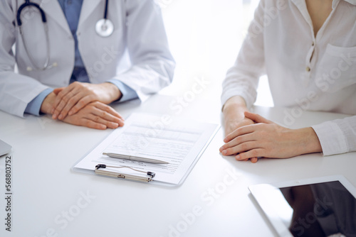 Fototapeta Naklejka Na Ścianę i Meble -  Doctor and patient discussing current health questions while sitting near of each other and using clipboard at the table in clinic, just hands closeup. Medicine concept