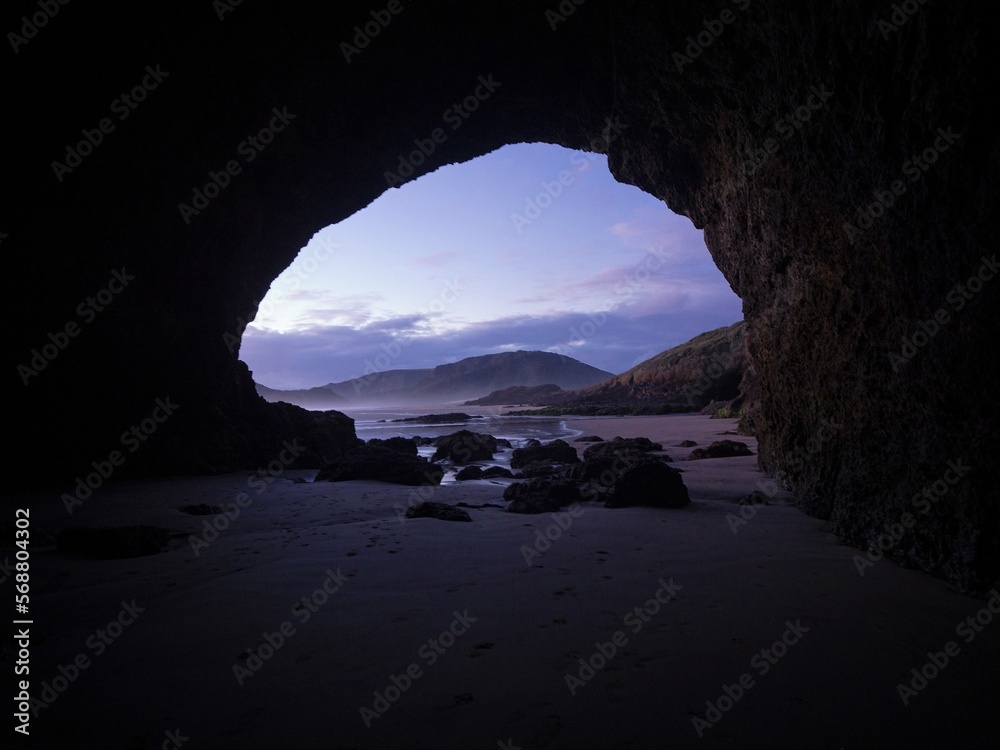 Looking out of a rock sea cave on idyllic black sand Te Henga Bethells beach during sunset in West Auckland New Zealand