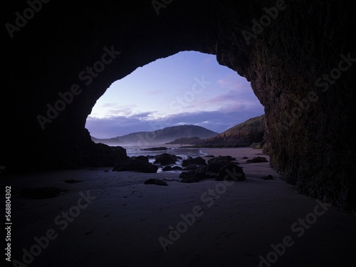 Looking out of a rock sea cave on idyllic black sand Te Henga Bethells beach during sunset in West Auckland New Zealand