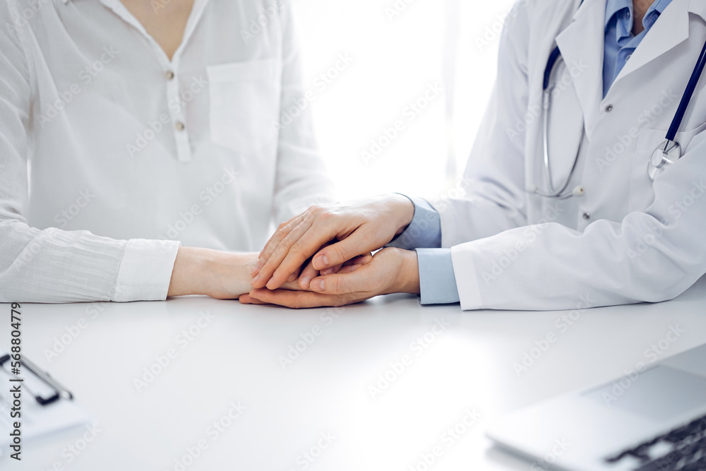 Doctor and patient sitting near each other at the table in clinic office. The focus is on female physician's hands reassuring woman, only hands, close up. Medicine concept Doctor and patient sitting near each other at the table in clinic office. The focus is on female physician's hands reassuring woman, only hands, close up. Medicine concept