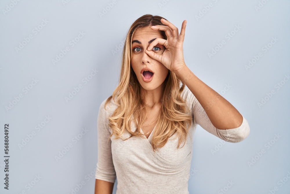 Young blonde woman standing over isolated background doing ok gesture shocked with surprised face, eye looking through fingers. unbelieving expression. Young blonde woman standing over isolated background doing ok gesture shocked with surprised face, eye looking through fingers. unbelieving expression.