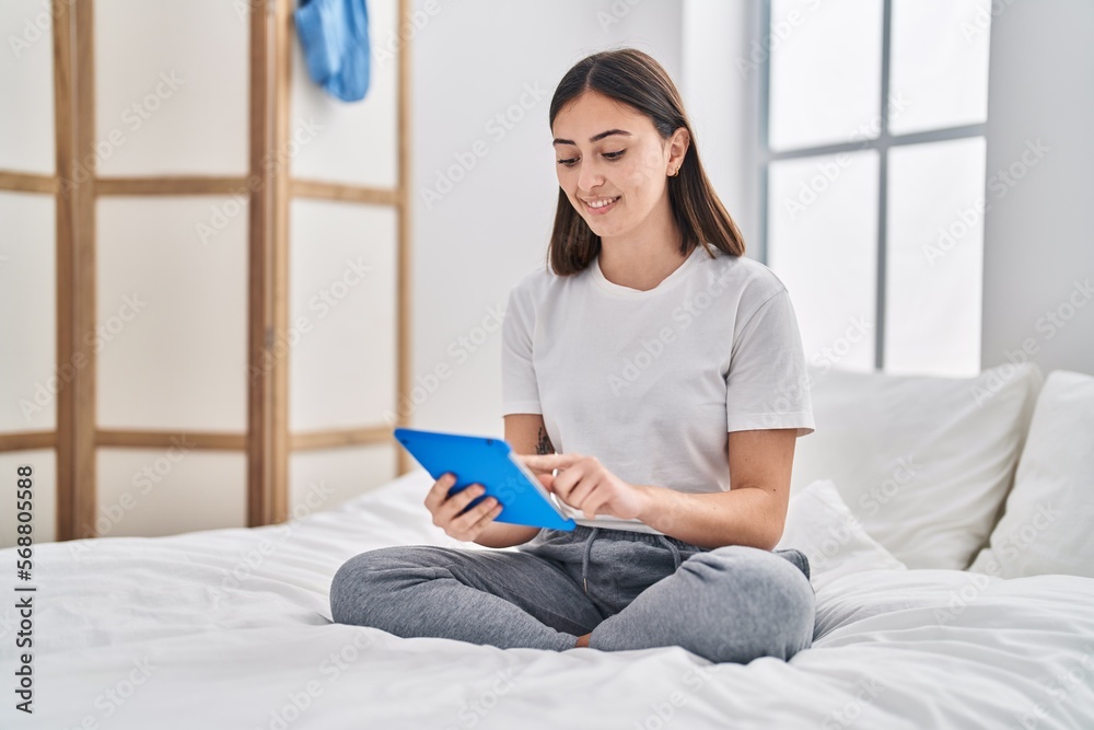 Young hispanic woman using touchpad sitting on bed at bedroom Young hispanic woman using touchpad sitting on bed at bedroom