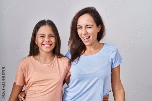 Young mother and daughter standing over white background winking looking at the camera with sexy expression, cheerful and happy face.