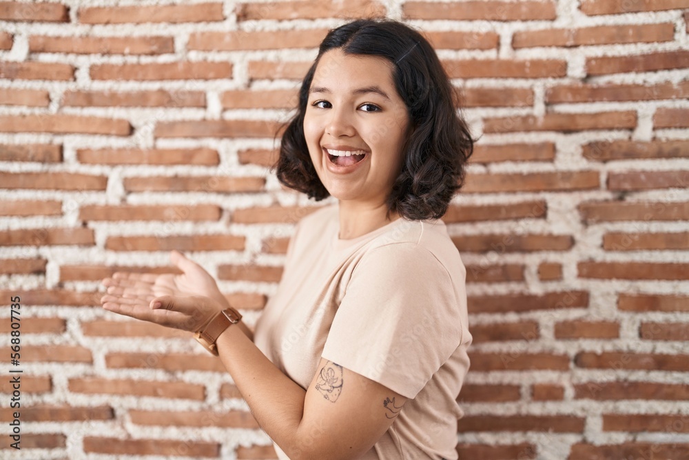 Young hispanic woman standing over bricks wall pointing aside with hands open palms showing copy space, presenting advertisement smiling excited happy Young hispanic woman standing over bricks wall pointing aside with hands open palms showing copy space, presenting advertisement smiling excited happy