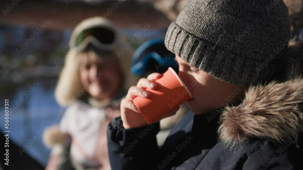 winter walk, charming male child in warm clothes enjoys drinking hot tea together with grandparents in forest backdrop of snow