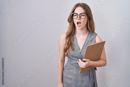 Caucasian woman wearing glasses and business clothes angry and mad screaming frustrated and furious, shouting with anger. rage and aggressive concept.
