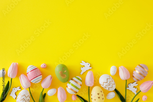 Easter decorations concept. Top view composition made of spring tulips, color eggs and cute easter bunnies on yellow background with empty space. Spring holiday card idea.