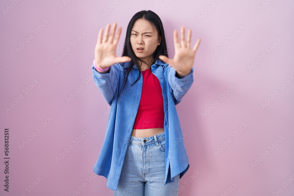 Young asian woman standing over pink background doing stop gesture with hands palms, angry and frustration expression Young asian woman standing over pink background doing stop gesture with hands palms, angry and frustration expression
