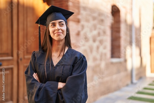 Young hispanic woman wearing graduated uniform standing with arms crossed gesture at university photo