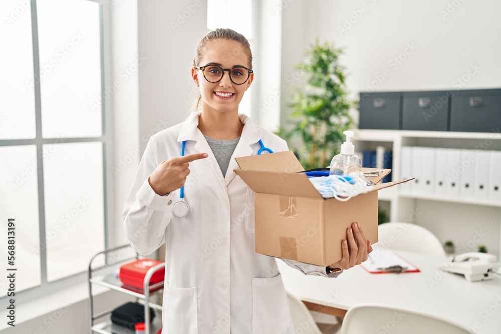 Young doctor woman holding box with medical items smiling happy pointing with hand and finger