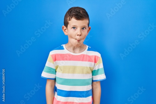 Young caucasian kid standing over blue background making fish face with lips, crazy and comical gesture. funny expression.