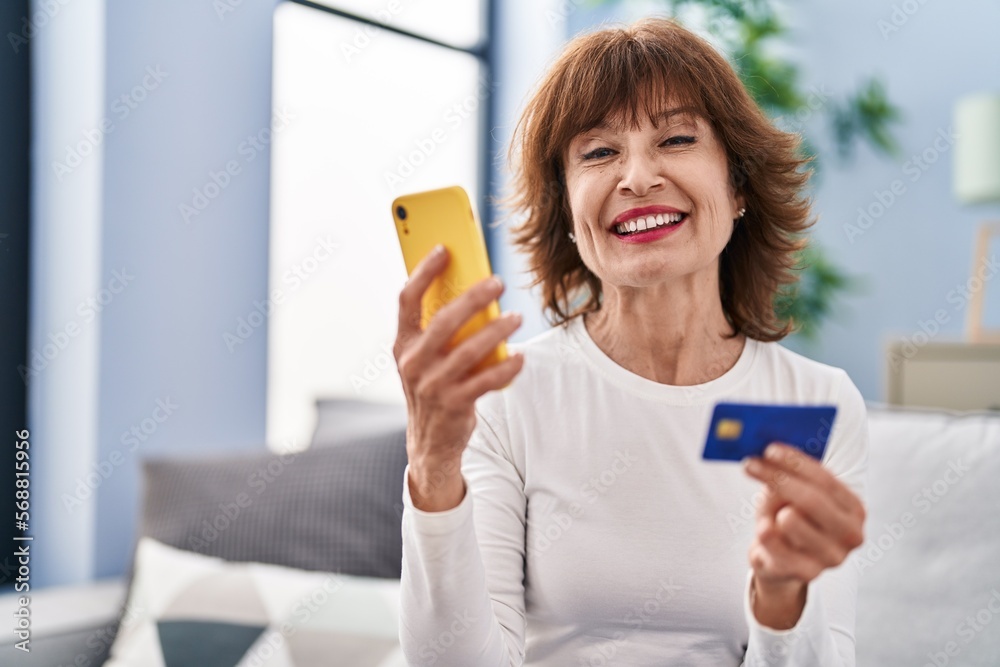Middle age woman using smartphone and credit card sitting on sofa at home Middle age woman using smartphone and credit card sitting on sofa at home