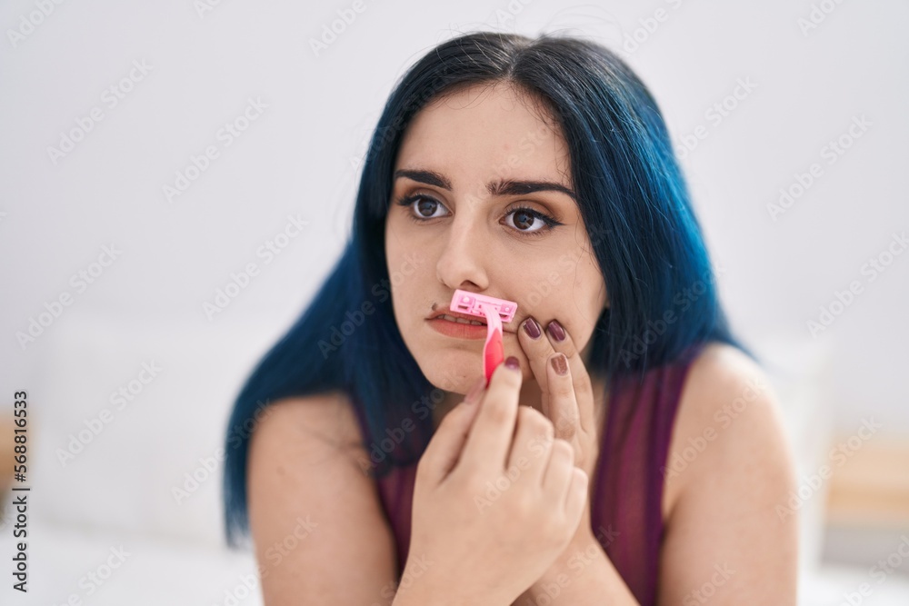Young caucasian woman sitting on bed shaving moustache with razor at bedroom Young caucasian woman sitting on bed shaving moustache with razor at bedroom