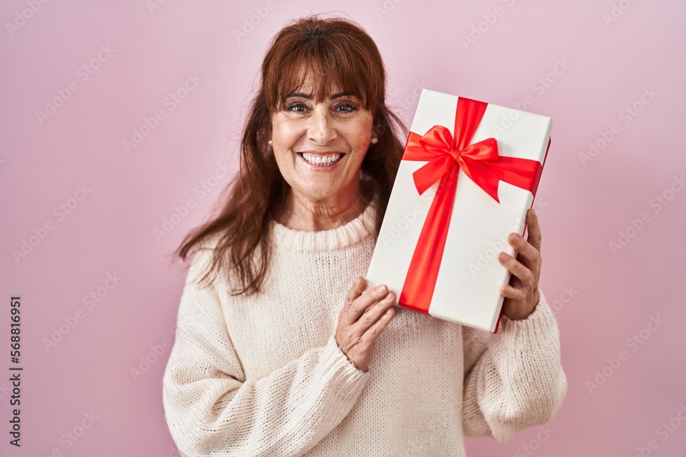 Middle age hispanic woman holding present smiling with a happy and cool smile on face. showing teeth. Middle age hispanic woman holding present smiling with a happy and cool smile on face. showing teeth.