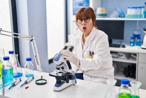 Middle age hispanic woman working at scientist laboratory scared and amazed with open mouth for surprise  disbelief face