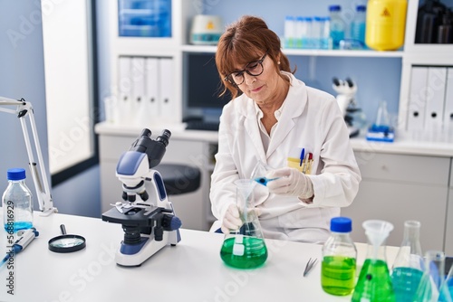 Middle age woman scientist measuring liquid at laboratory