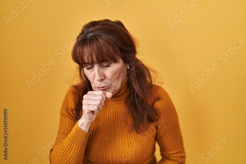 Middle age hispanic woman standing over yellow background feeling unwell and coughing as symptom for cold or bronchitis. health care concept.