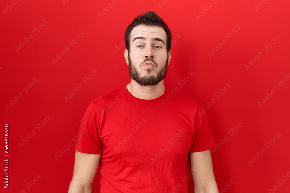 Young hispanic man wearing casual red t shirt looking at the camera blowing a kiss on air being lovely and sexy. love expression. Young hispanic man wearing casual red t shirt looking at the camera blowing a kiss on air being lovely and sexy. love expression.