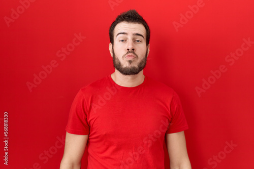 Young hispanic man wearing casual red t shirt looking at the camera blowing a kiss on air being lovely and sexy. love expression.