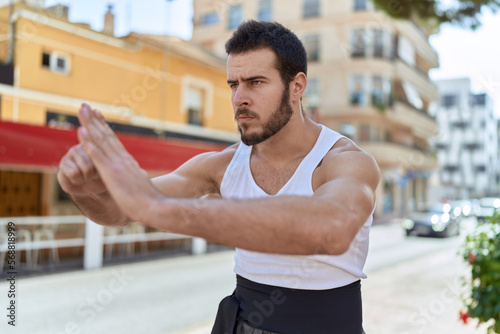 Young hispanic man karate fighter doing combat salute at street
