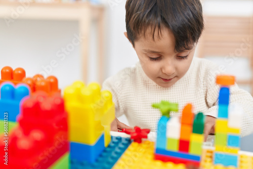 Adorable hispanic boy playing with construction blocks sitting on table at kindergarten
