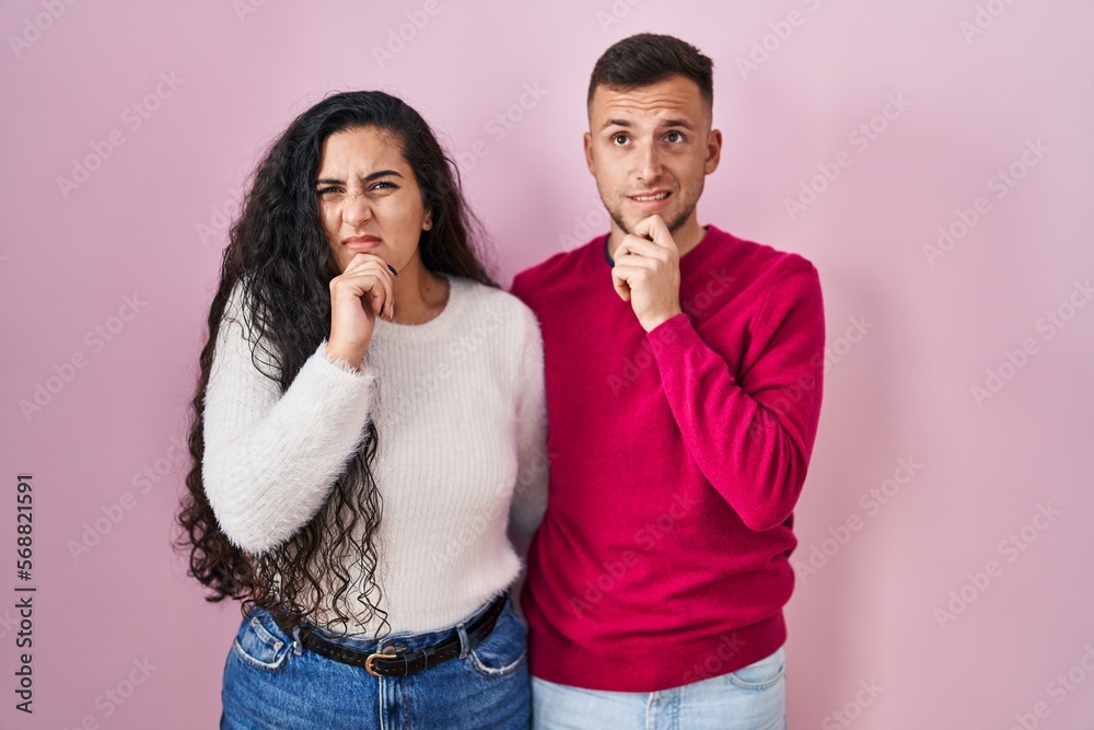 Young hispanic couple standing over pink background thinking worried about a question, concerned and nervous with hand on chin Young hispanic couple standing over pink background thinking worried about a question, concerned and nervous with hand on chin