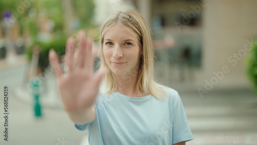 Young blonde woman doing stop gesture with hand at street