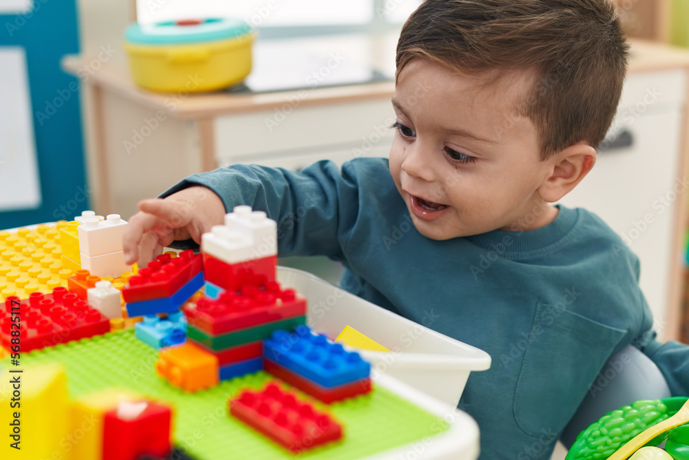 Adorable hispanic boy playing with construction blocks sitting on table at kindergarten Adorable hispanic boy playing with construction blocks sitting on table at kindergarten