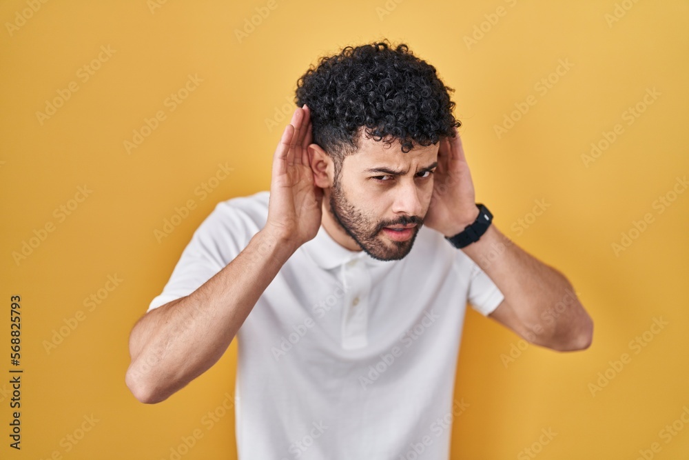 Arab man standing over yellow background trying to hear both hands on ear gesture, curious for gossip. hearing problem, deaf Arab man standing over yellow background trying to hear both hands on ear gesture, curious for gossip. hearing problem, deaf