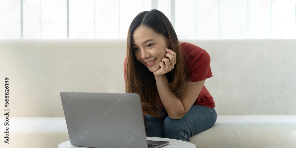 An attractive young woman is working on a laptop while sitting on sofa at home An attractive young woman is working on a laptop while sitting on sofa at home
