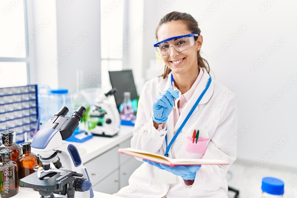 © Krakenimages.com - Young hispanic woman wearing scientist uniform writing on notebook at laboratory © Krakenimages.com - Young hispanic woman wearing scientist uniform writing on notebook at laboratory