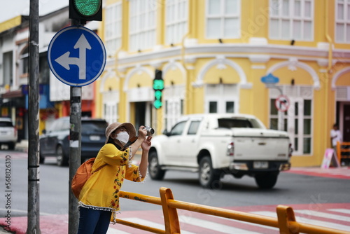 Tourists use digital cameras to take pictures at beauty of city streets old town in old phuket town,Thailand. Woman wearing yellow top and wide-brimmed hat, sling an orange backpack walking happily. 
