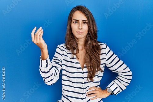 Young hispanic woman standing over blue isolated background doing italian gesture with hand and fingers confident expression