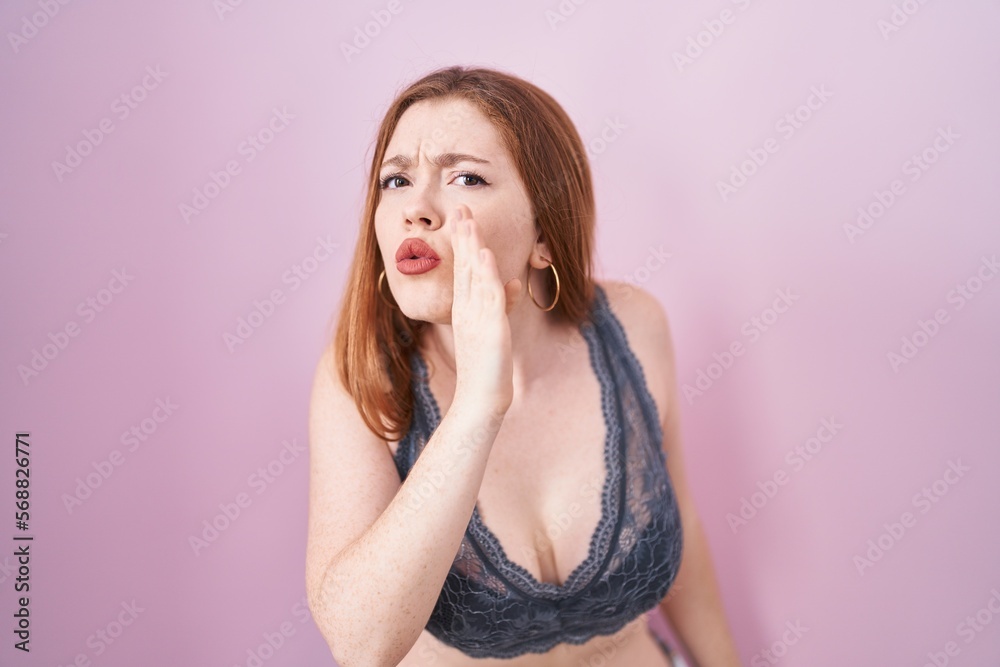 Redhead woman wearing lingerie over pink background hand on mouth telling secret rumor, whispering malicious talk conversation Redhead woman wearing lingerie over pink background hand on mouth telling secret rumor, whispering malicious talk conversation