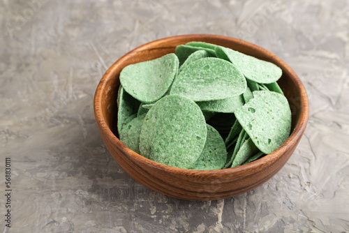 green potato chips with herbs on gray concrete background. Side view, close up.