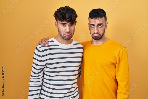 Young hispanic gay couple standing over yellow background depressed and worry for distress, crying angry and afraid. sad expression.