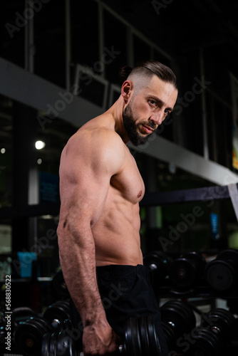 A brutal muscular bearded man with abs holds a dumbbell in the gym. Active lifestyle, sports