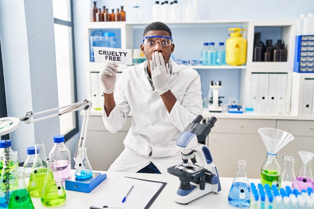 African american man working on cruelty free laboratory covering mouth with hand, shocked and afraid for mistake. surprised expression African american man working on cruelty free laboratory covering mouth with hand, shocked and afraid for mistake. surprised expression