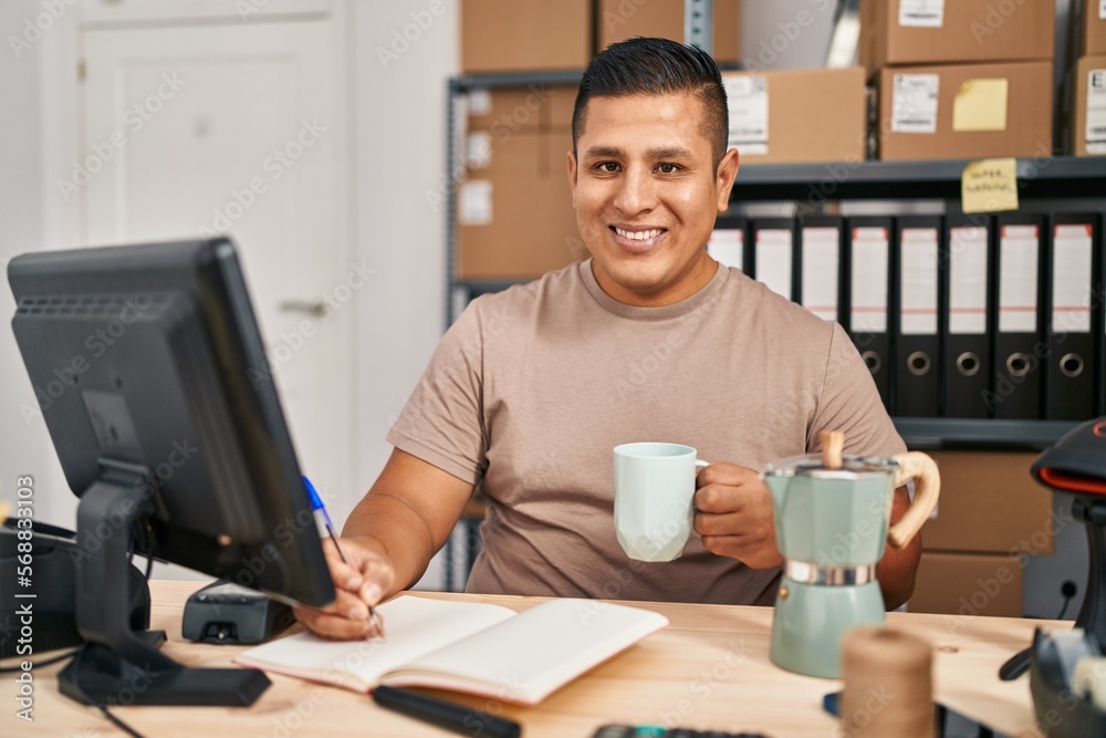 Young latin man ecommerce business worker drinking coffee writing on notebook at office Young latin man ecommerce business worker drinking coffee writing on notebook at office