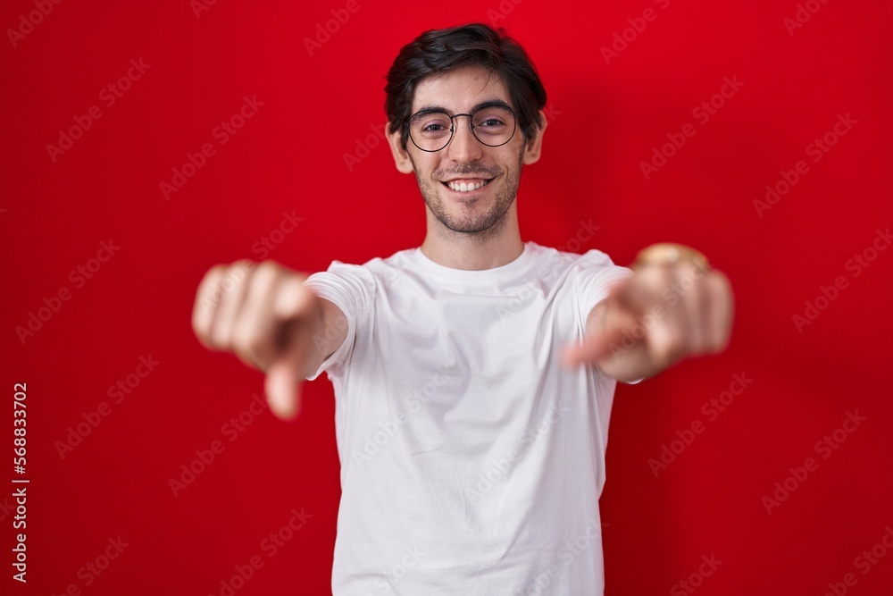Young hispanic man standing over red background pointing to you and the camera with fingers, smiling positive and cheerful Young hispanic man standing over red background pointing to you and the camera with fingers, smiling positive and cheerful