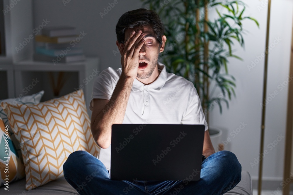Young hispanic man using laptop at home at night yawning tired covering half face, eye and mouth with hand. face hurts in pain. Young hispanic man using laptop at home at night yawning tired covering half face, eye and mouth with hand. face hurts in pain.
