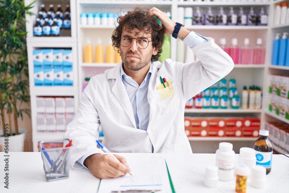 Hispanic young man working at pharmacy drugstore confuse and wondering about question. uncertain with doubt, thinking with hand on head. pensive concept. Hispanic young man working at pharmacy drugstore confuse and wondering about question. uncertain with doubt, thinking with hand on head. pensive concept.