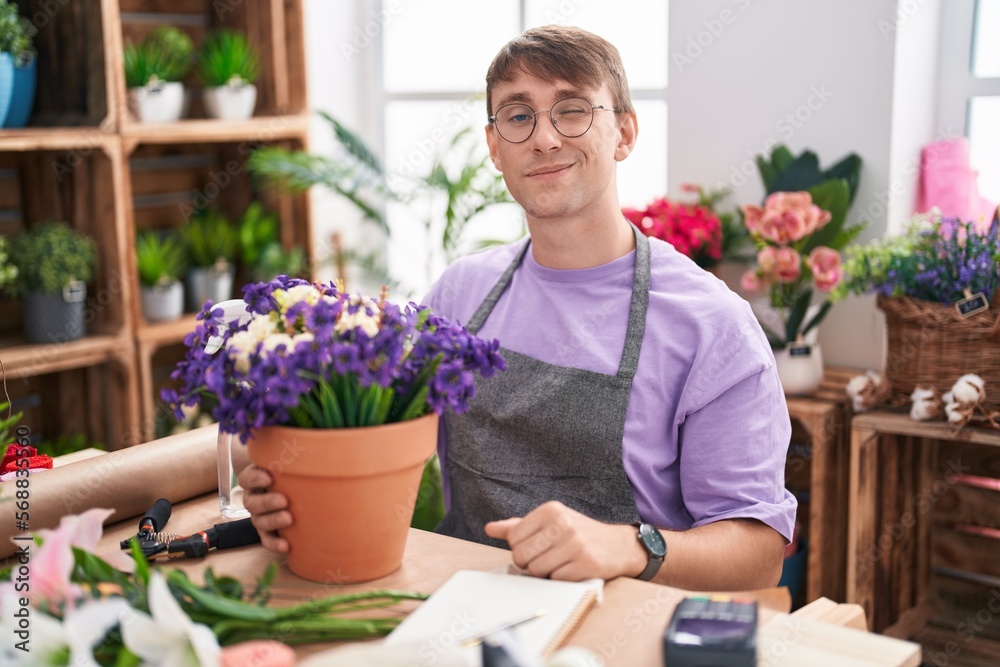 Caucasian blond man working at florist shop winking looking at the camera with sexy expression, cheerful and happy face.