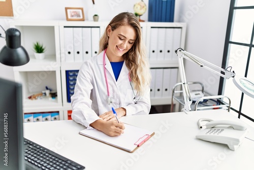 Young woman wearing doctor uniform writing on document at clinic