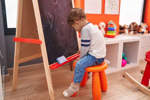 Adorable caucasian boy preschool student sitting on chair drawing on blackboard at kindergarten