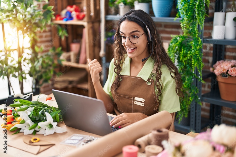 Young hispanic woman working at florist shop doing video call pointing thumb up to the side smiling happy with open mouth Young hispanic woman working at florist shop doing video call pointing thumb up to the side smiling happy with open mouth