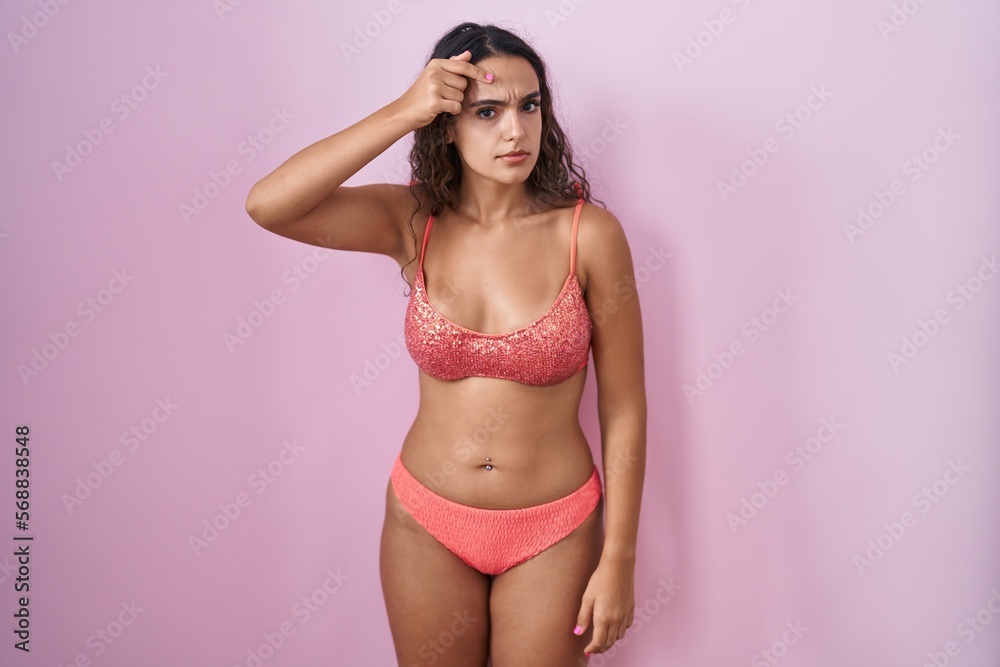 Obraz premium Young hispanic woman wearing lingerie over pink background pointing unhappy to pimple on forehead, ugly infection of blackhead. acne and skin problem