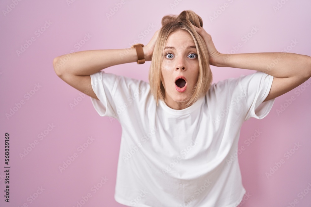 Young caucasian woman standing over pink background crazy and scared with hands on head, afraid and surprised of shock with open mouth Young caucasian woman standing over pink background crazy and scared with hands on head, afraid and surprised of shock with open mouth